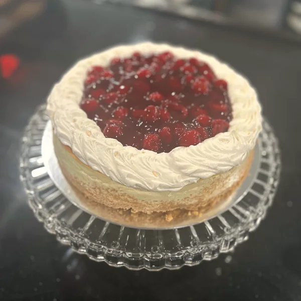 A cheesecake topped with cherry filling on a glass stand