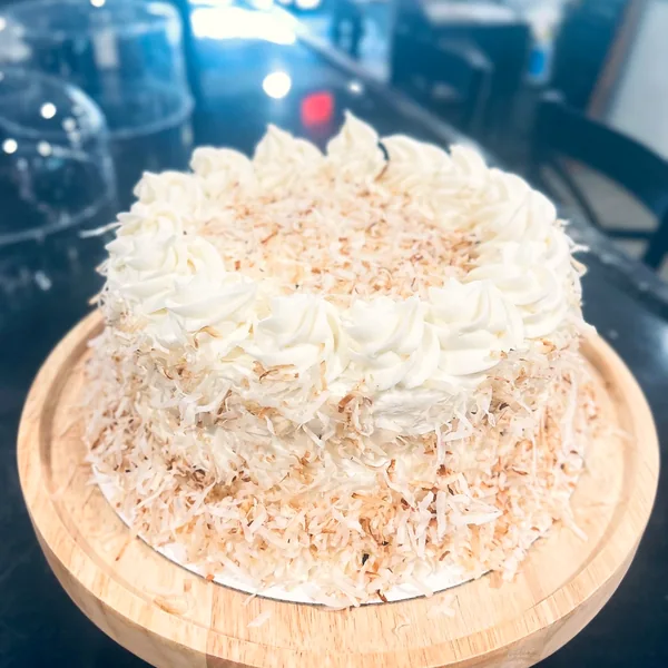 A coconut-covered layer cake on a wood board