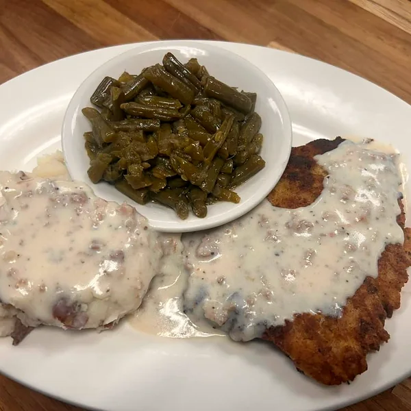 A lunch plate of breaded chicken smothered in white gravy with green beans